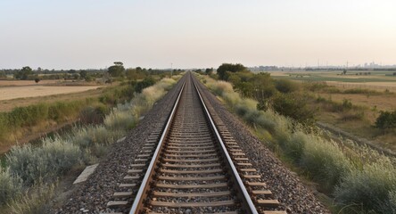 Obraz premium Long stretch of train tracks bordered by small bushes and open fields
