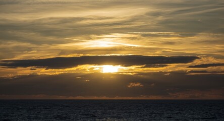Obraz premium Expansive seaside sky at sunset with sun shining through layered clouds nature scene