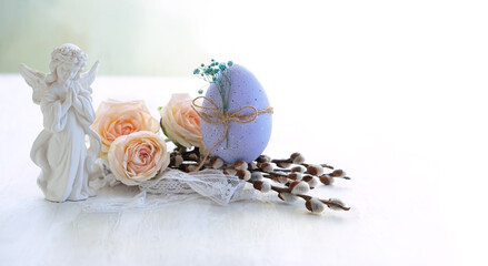 Fototapeta premium Easter holiday background. Beautiful angel figurine with easter egg, pussy willow and rose flowers on light table close up. symbol of Easter, Christianity religion, faith in God, prayer. soft focus