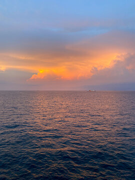 View of a ferry crossing the ocean with orange cumulonimbus clouds at sunset in Indonesian waters.