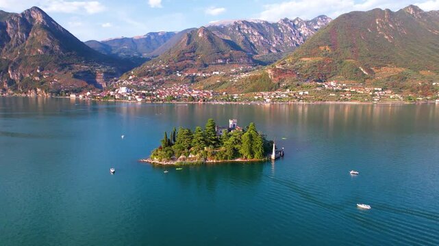 Isola di Loreto Iseo Lake Lombardy Italy 4K Aerial. Drone panorama of fairy tale island castle with neo Gothic fortress and green trees in blue water. Authentic secret travel hidden gems asset