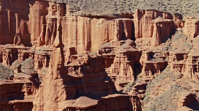 Eroded rock formations create a stunning desert landscape in Kyrgyzstan. Orbiting telephoto drone view. Rugged terrain showcases natural beauty under sunny skies.