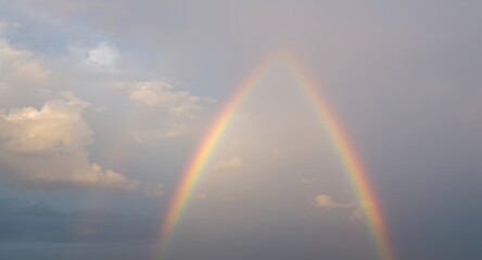 Fototapeta premium Shimmering rainbow spanning a calm sky with pastel cloud surrounds and serene watercolor brushwork
