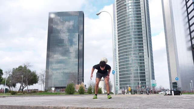 Talented soccer player skillfully balancing and juggling a ball with his head and neck in a modern urban park with skyscrapers behind
