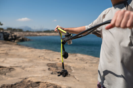 Close-up of a man's hands holding a scuba diving regulator and yellow hose against a coastal background. Safety check, preparing equipment, nautical gear, water sports adventure.