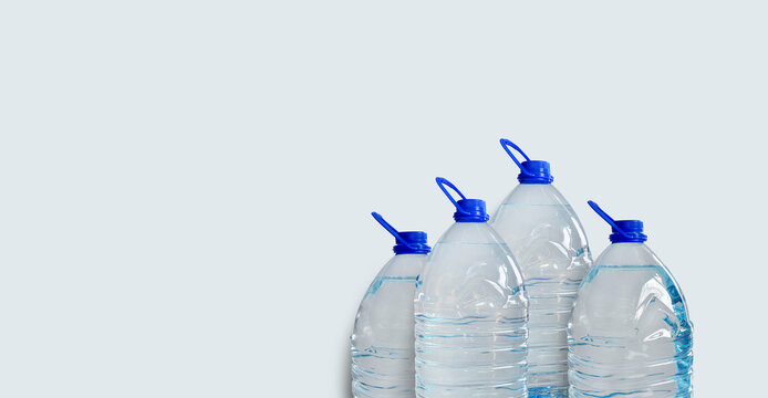 Drinking water bottles, isolated on light blue backdrop. Transparent plastic 5l bottles, full, blue cap. Clean water supply concept. Horizontal studio shot