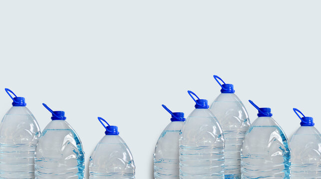 Drinking water bottles, isolated on light blue backdrop. Transparent plastic 5l bottles, full, blue cap. Clean water supply concept. Horizontal studio shot