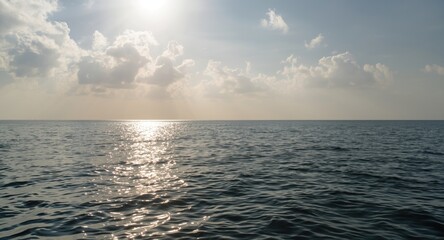 Obraz premium Mild sea surface shining under sunlight with calm ripples and a peaceful cloudy sky