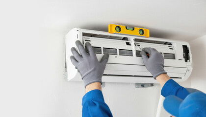 Technician installing air conditioner unit on white wall. Man worker using spirit level tool for precise indoor mounting. Professional HVAC climate control system maintenance concept.