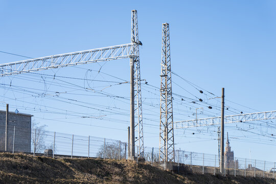 Urban railway power line structures with catenary cables, fenced trackside corridor and distant city tower, energy distribution and public transport network concept