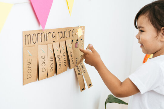 Little girl checking morning routine chart at home - Kid using DIY chore schedule - Learning and child development concept
