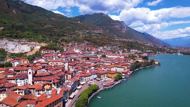 Italy Lake Iseo Lovere town aerial drone flight back. Red roofs and medieval towers with sail boats on water. One of the most beautiful villages in Italy Alps mountain travel scenery 4k video