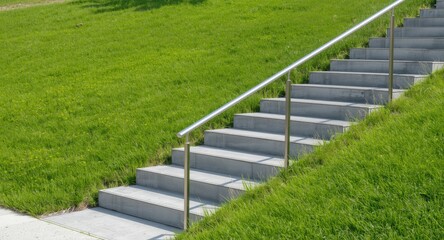 Obraz premium Modern concrete staircase with stainless steel railing on bright green grass lawn under summer sun