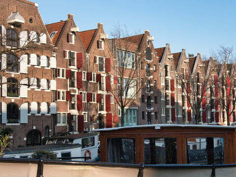 Row of Dutch Gable Houses with Red Shutters - Historic row of traditional Amsterdam canal houses featuring distinctive stepped gables, red and white shutters, and a houseboat in the foreground.