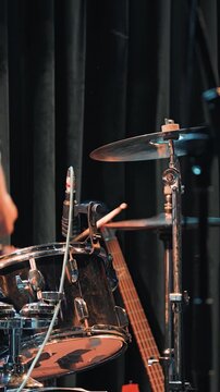 Dynamic close up of a rock band performing live. A musician's hair is a motion blur from headbanging next to a guitar and chrome drum kit. Warm stage lights create an energetic, intense atmosphere