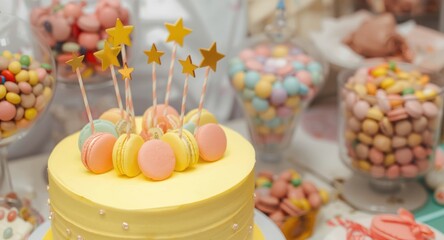 Fototapeta premium Joyful yellow birthday cake topped with star decorations and macarons at a candy buffet