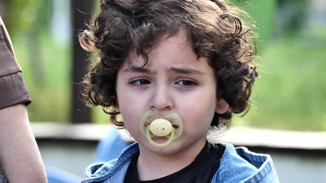 Armenian boy with curly hair and pacifier, thinking outdoors