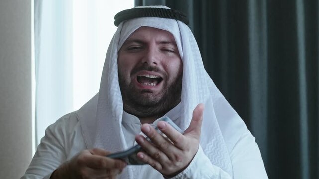 An Arabic man throws hundred-dollar banknotes and smiles. Rich prince who buys everything