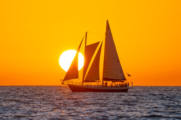 Fototapeta premium Sunset and Sailing yacht, Sailboat. Ocean sunset tour. Bright sun and warm orange sky. Calm sea, soft waves create a peaceful travel and vacation scene with relaxing coastal atmosphere. Gulf of Mexico