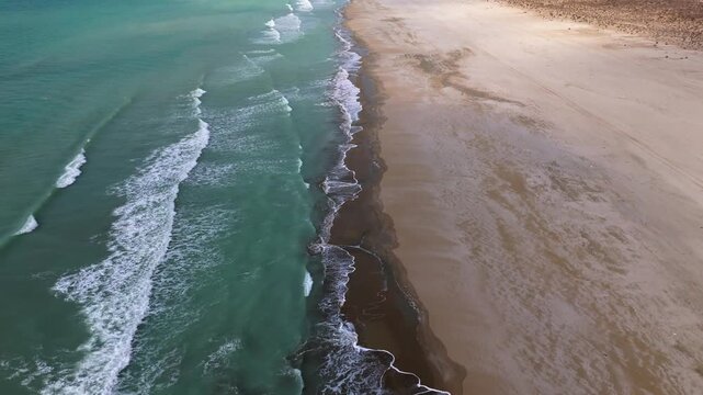 Drone pullback shot of an empty Caspian Sea beach with turquoise waves washing over a brown yellow sandy shore no buildings or vehicles visible wide natural seascape with vibrant colors and dynamic