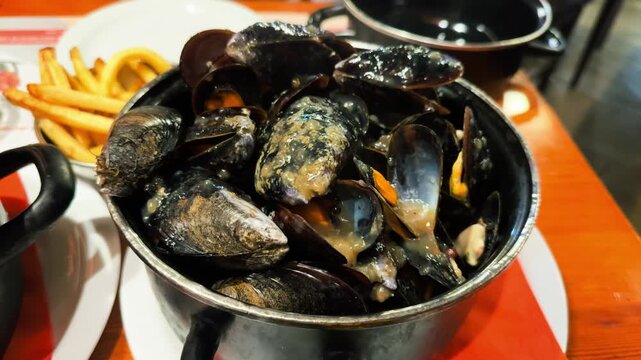 A restaurant specializing in mussels serves a pot of mussels cooked in a spicy sauce with French fries. High quality 4k footage