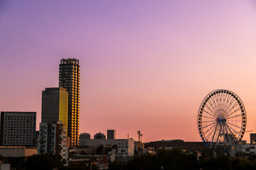 Modern skyline featuring Estrella de Puebla Ferris wheel and illuminated skyscrapers against vibrant purple and pink sunset sky in Puebla, Mexico © simonmayer