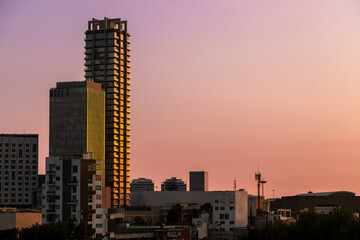 Modern skyscrapers with glass and concrete facades illuminated by golden sunset light against vibrant pink and orange sky in Puebla, Mexico © simonmayer