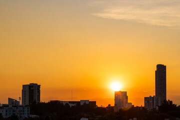 Bright sun setting behind modern buildings casting silhouettes against vibrant orange sky in Puebla, Mexico © simonmayer