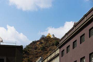 Obraz premium View of yellow Chapel of San Miguel Arcangel atop dry hill overlooking colorful urban buildings under blue sky with clouds in Atlixco, Puebla, Mexico