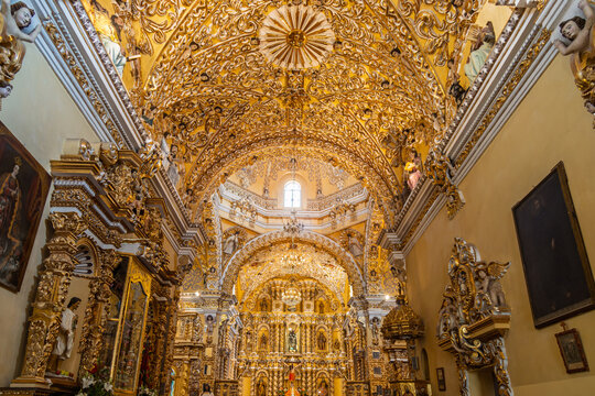 Opulent golden baroque interior of San Francisco Acatepec church featuring ornate vaulted ceiling covered in carvings of angels and cherubs with grand crystal chandeliers in Cholula, Puebla, Mexico