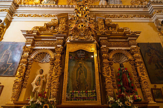 Ornate golden baroque retable featuring Virgin of Guadalupe flanked by statues of Saint Juan Diego and another Virgin Mary adorned with flowers inside historic church