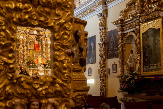 Crucifix of Jesus Christ reflected in an ornate golden baroque mirror with statues of Virgin of Guadalupe and Saint Juan Diego on side altar in Cholula, Puebla, Mexico