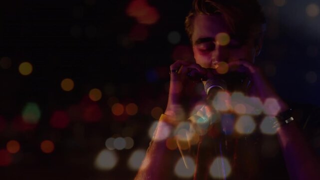 Animation of blurred night road traffic over caucasian man playing harmonica on concert