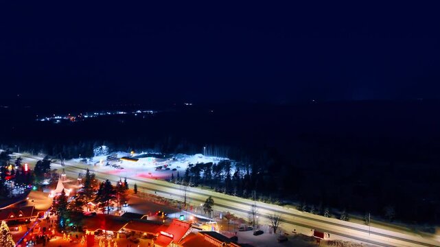 Footage over the gorgeous luminous Santa Claus village. Approaching the dark area of the vast forest at night.