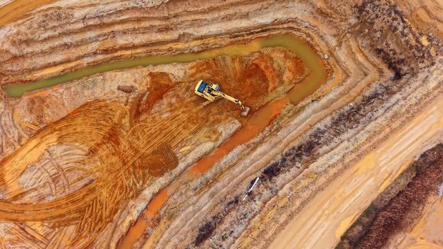 Yellow excavator picking sand in the quarry. Truck loaded with sand moves by the ground road. Borrow pit from aerial view.