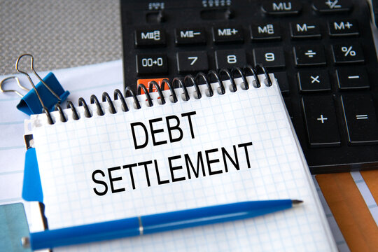 Notebook with the words DEBT SETTLEMENT in the notebook on the background of a black calculator