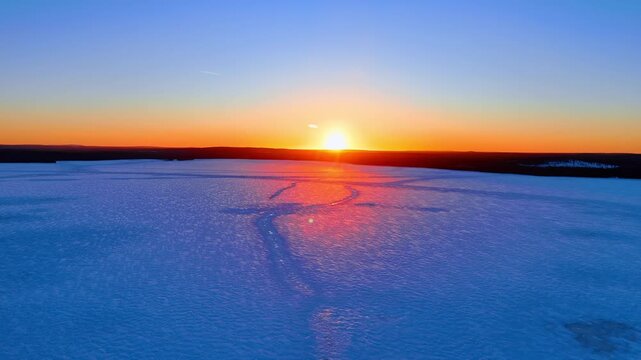 Flying over the vast snow field lit by the setting sun. Sunset in the wilderness in Lapland, Finland.