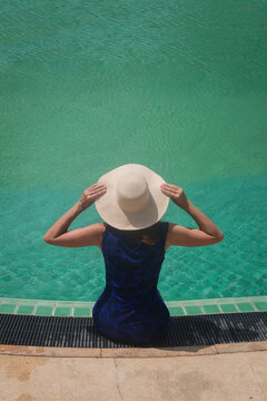 abstract background of woman with sunhat sitting on edge of swimming pool 