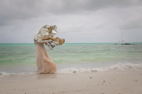abstract portrait of woman in dress on beach with silver foil in the wind