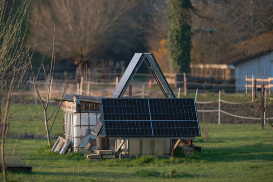DIY solar panel system installed in backyard garden,  photovoltaic panels mounted on simple wooden structure supported by water containers. DIY off-grid solar panel setup in rural backyard garden.