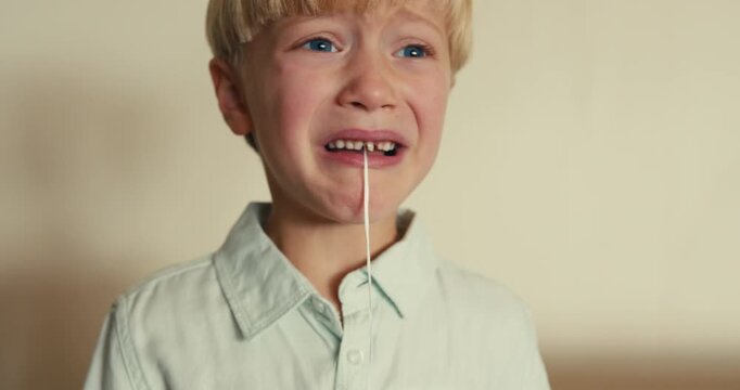 Close-up of a boy with dental floss tied to a loose baby tooth. He is scared and crying, wanting to pull it out but afraid to do so.
