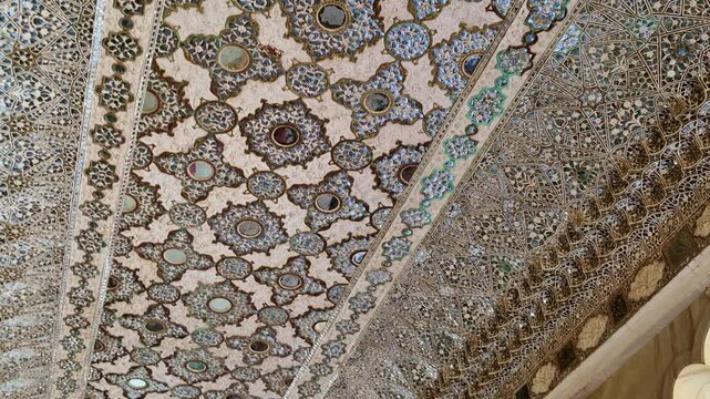 Showing the Sheesh Mahal inside Amer Fort with mirror-work ceiling, intricate glass mosaics, and carved marble arches opening toward the courtyard with a domed pavilion visible outside.