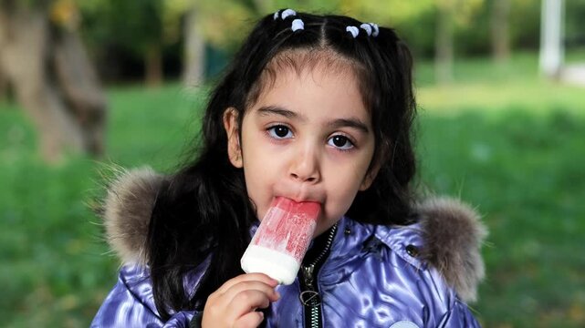 Armenian child eating red and white popsicle outdoors in a purple winter coat