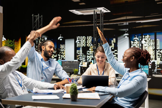 Doing high five hand gesture, excitement and staff members in diverse startup office making progress on project. Celebrating , successful business audit and delighted coworkers working late at night
