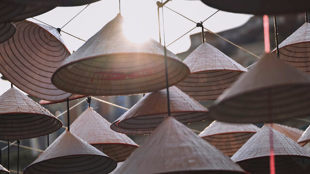 Traditional Asian conical hats hanging outdoors against a bright sun
