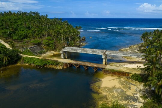 Aerial view of Maasin Bridge and the palm-fringed Maasin River in Siargao. Scenic red bridge crossing through a dense tropical coconut forest, Philippines