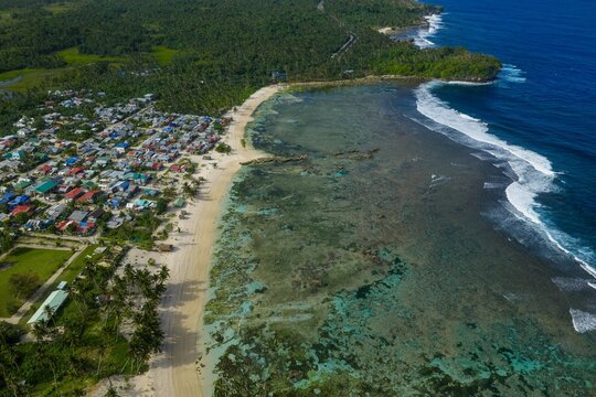 Aerial view of Caridad Beach in Siargao. Pristine white sand shoreline bordered by a vast coconut palm plantation and turquoise Pacific Ocean, Philippines