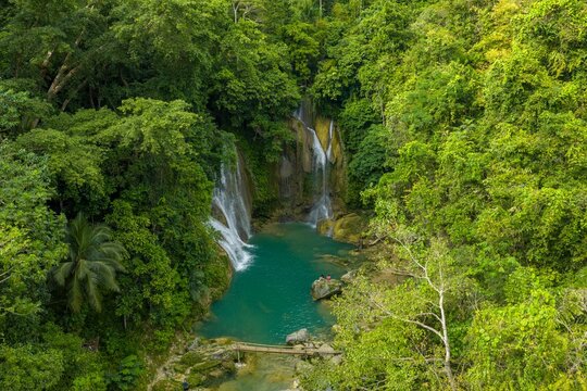 Aerial view of Pahangog Twin Falls in Dimiao, Bohol. Two majestic waterfalls cascading into a vibrant turquoise natural pool surrounded by dense tropical jungle.