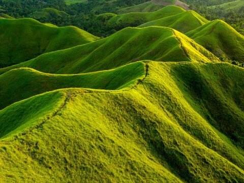 Aerial sunrise over Alicia Panoramic Park, Bohol. Rolling green ridges of Binabaje Hills under golden light, scenic tropical mountain landscape in the Philippines.