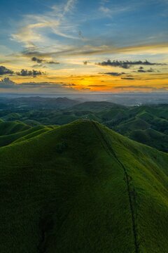 Aerial sunrise over Alicia Panoramic Park, Bohol. Rolling green ridges of Binabaje Hills under golden light, scenic tropical mountain landscape in the Philippines.